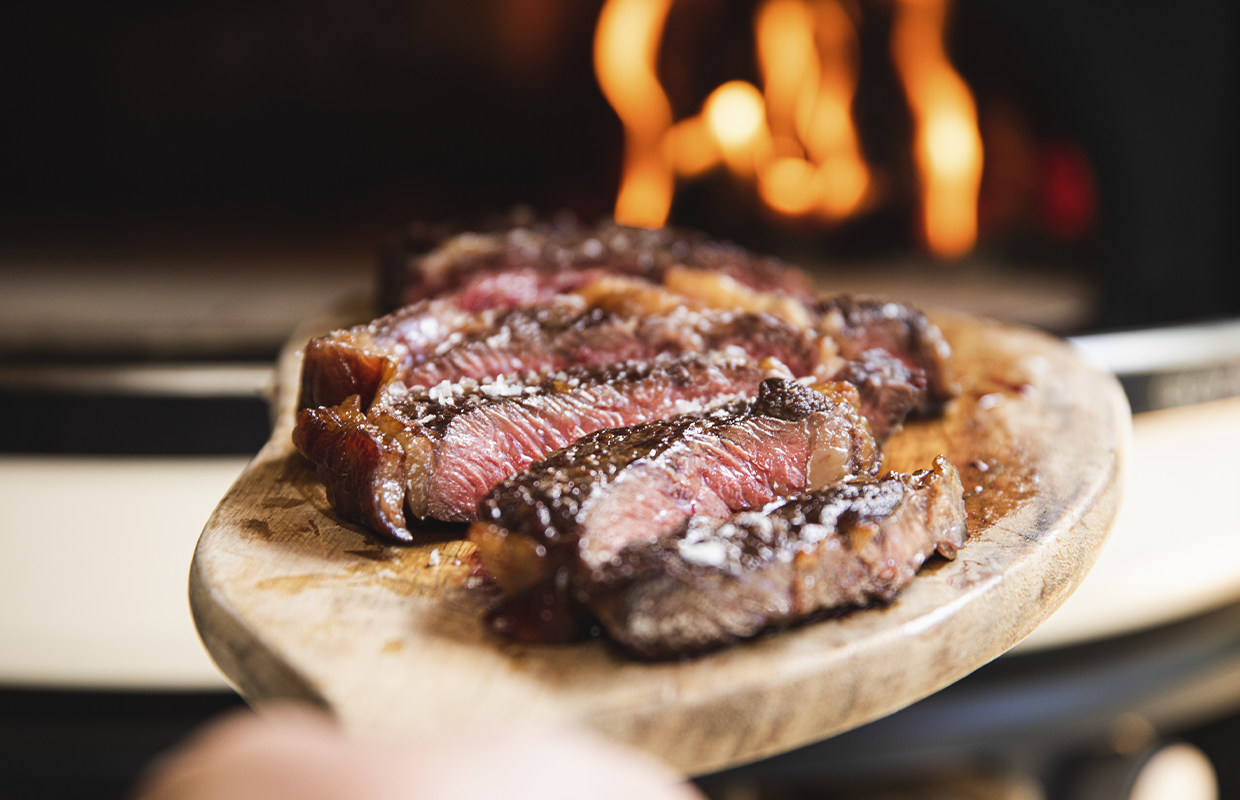 steak cut up on block in front of pizza oven