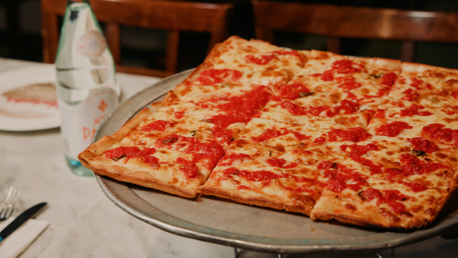 thin crust pizza on a pizza tray with a sparking water next to it.